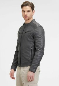 Giacca in pelle nera con un design aderente, caratterizzata da tasche con zip e dettagli a costine sulle spalle. Texture liscia con colletto strutturato.
