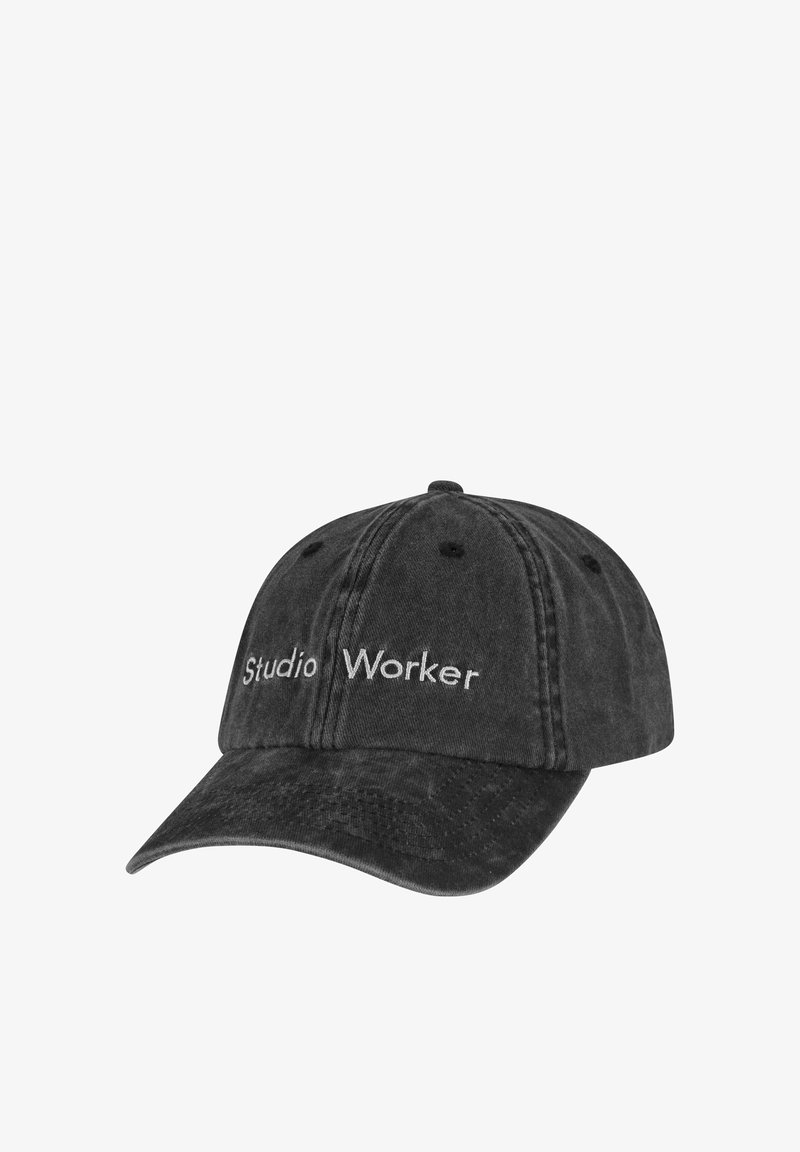 Melnas kokvilnas beisbola cepures ar izliekto malu, uz priekšu ar baltiem izšūtiem vārdiem "Studijas Strādnieks" un redzamām šuvju detalēm.