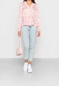 Blusa peplum rosa chiaro con motivo floreale, colletto arricciato, maniche lunghe; abbinata a jeans azzurri e una piccola borsa floreale.