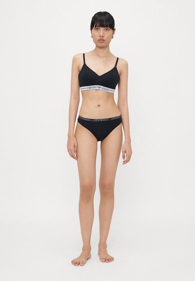 Set bikini nero composto da un bralette con spalline sottili e fascia brandizzata, abbinato a slip in stile hipster, entrambi in tessuto liscio.