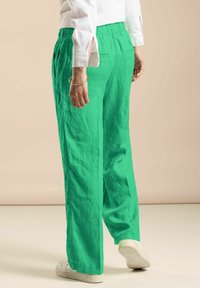 Green linen trousers with a relaxed fit, featuring an elastic waistband, side pockets, and subtle texture, paired with white sneakers.