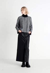Maglione herringbone grigio e nero con scollatura alta abbinato a una gonna maxi in pelle nera con spacco frontale e stivali neri robusti.