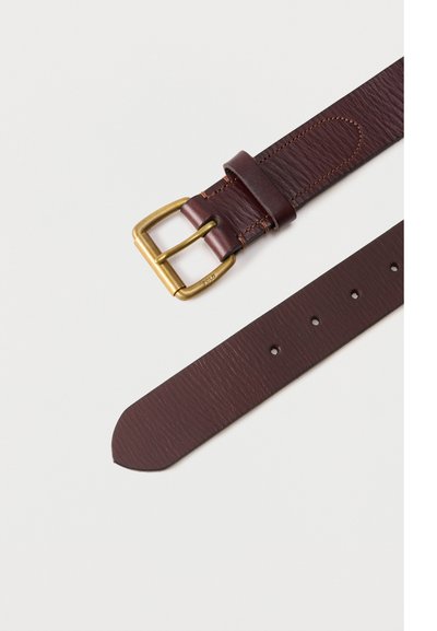 Sötétbarna bőröv rézcsattal és több állítólyukkal fehér háttéren.