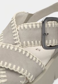 Γκρι σουέντ σανδάλι με σχεδιασμό με σταυρωτό λουράκι, ραφές σε κρεμ χρώμα, μεταλλικό αγκράφα και χοντρή σόλα με πλατφόρμα.