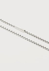 Ασημένιου τόνου μεταλλική αλυσίδα κολιέ με ορθογώνιο κούμπωμα που έχει σχέδιο σταυρωτό σε ανοιχτό φόντο.