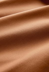 Tekstureeritud kangas soojas, keskmises pruuni varjus, millel on peen sära. Sile viimistlus kortsudega, mis näitavad pehmust ja paindlikkust.