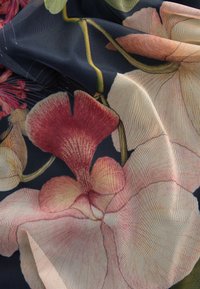 Tissu noir transparent avec une fine texture en maille présentant de grands motifs floraux roses et rouges et des tiges vertes.
