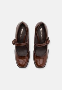 Paire de chaussures Mary Jane en cuir verni marron avec bouts carrés et brides à boucle, vues de dessus sur fond blanc.