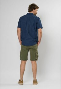 Korte mouwen, donkerblauw shirt met een subtiele textuur, gecombineerd met olijfgroene cargoshorts met zijzakken. Tan sneakers maken de look af.