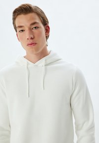 Witte hoodie van zacht materiaal, met een kangoeroezak, trekkoorden en een ontspannen pasvorm. Soepele textuur met minimale naden.