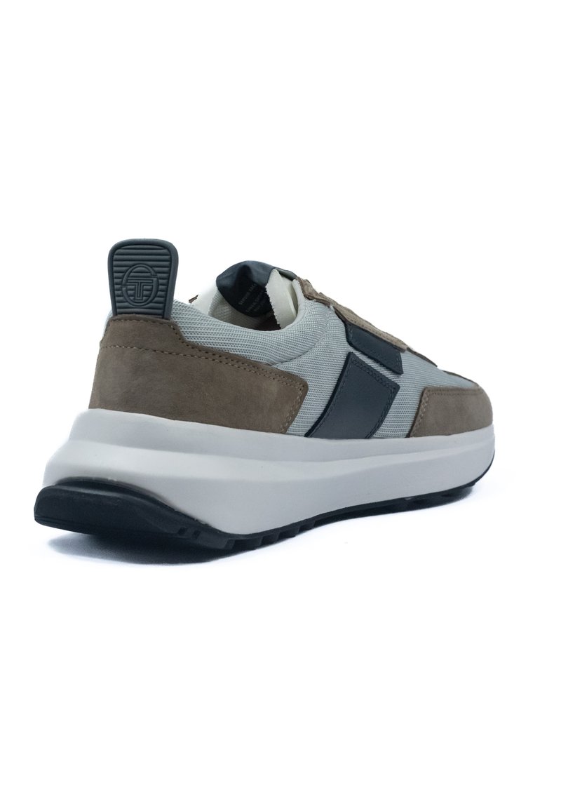 Zapatillas con una parte superior de malla gris, acentos de ante marrón, detalles en negro y una suela blanca gruesa. Banda en la parte trasera para facilitar el uso.