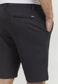 Shorts en coton noir mélangé avec une coupe slim, dotés d'une poche arrière avec un bouton et d'un discret accent logo. Texture lisse ; design arrivant au genou.