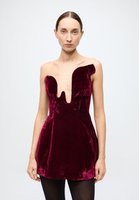 Burgundy velvet mini dress with a deep neckline cutout. Fitted bodice and flared skirt, featuring a slight asymmetrical shoulder design.