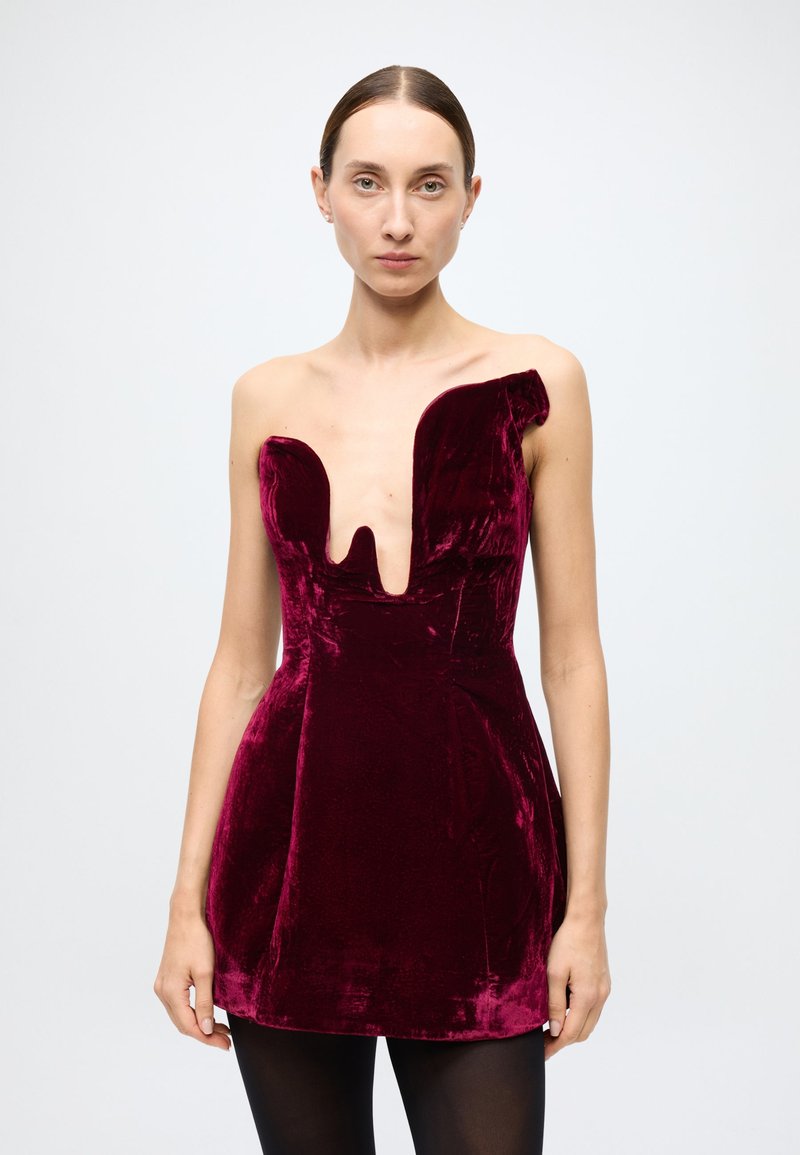 Burgundy velvet mini dress with a deep neckline cutout. Fitted bodice and flared skirt, featuring a slight asymmetrical shoulder design.