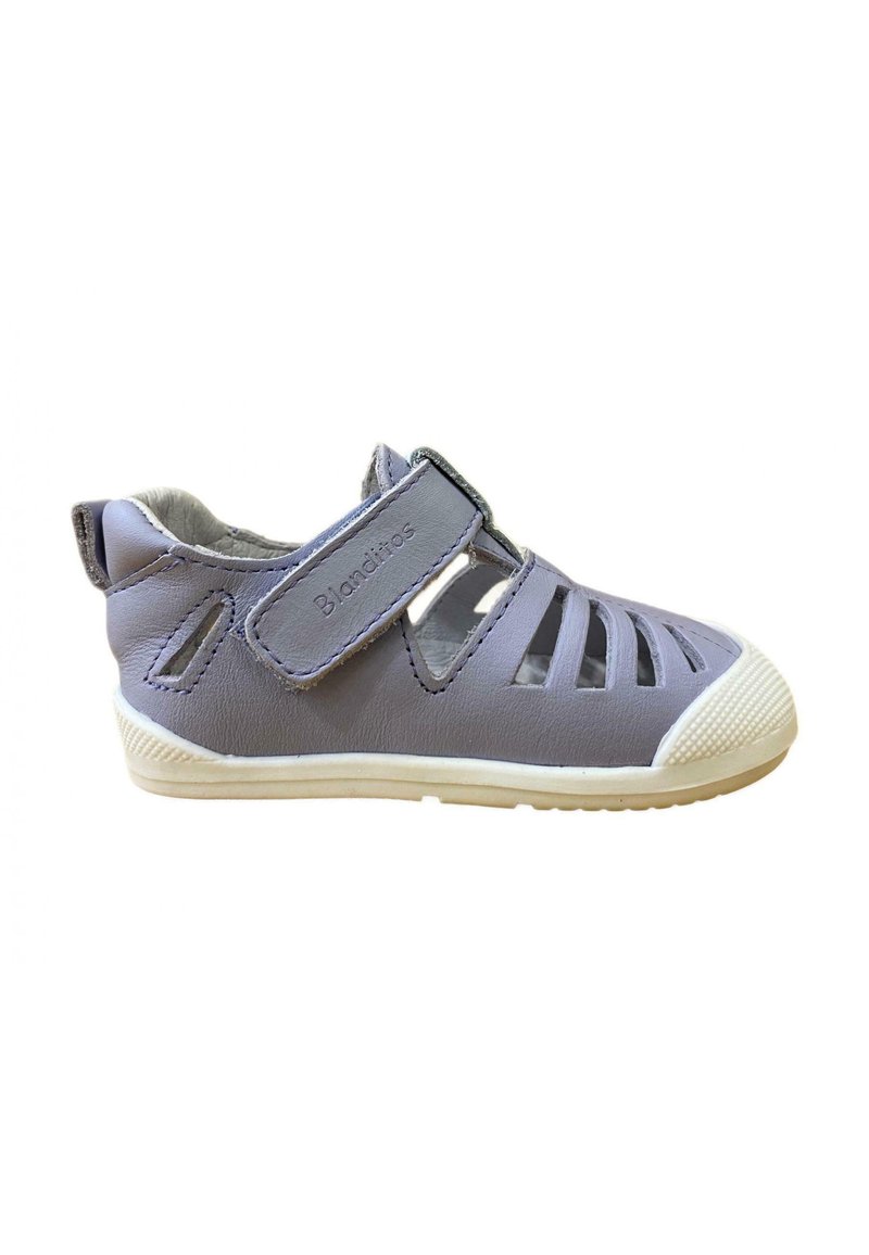 Sandalia de cuero gris con diseño recortado, correa ajustable de Velcro y suela de goma blanca. Presenta una tapa de toe texturizada y un lado con marca.