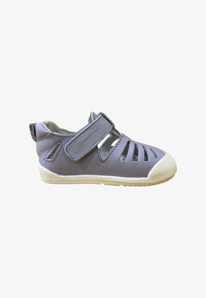 Sandalia de cuero gris con diseño recortado, correa ajustable de Velcro y suela de goma blanca. Presenta una tapa de toe texturizada y un lado con marca.