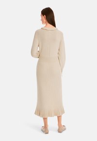 Strickkleid in hellbeige mit strukturierter Rippoptik, einem rüschigen Kragen und einem ausgestellten Saum. Mit langen Ärmeln und einer taillierten Passform.