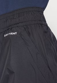 Crne vodootporne hlače s elastičnom trakom u struku, s "DRYVENT" logom u bijeloj boji. Glatka tekstura, lagani materijal i kutevi na šavovima.