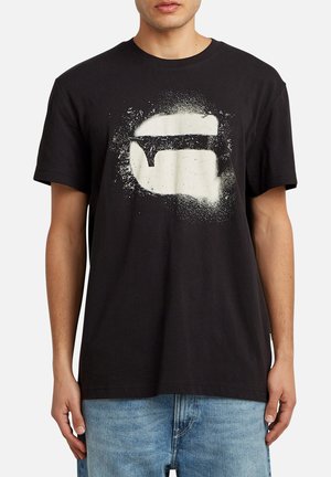 Camiseta de algodón negra con un gran diseño gráfico blanco que se asemeja a unos labios con un efecto de salpicadura texturizada. Manga corta y cuello redondo.