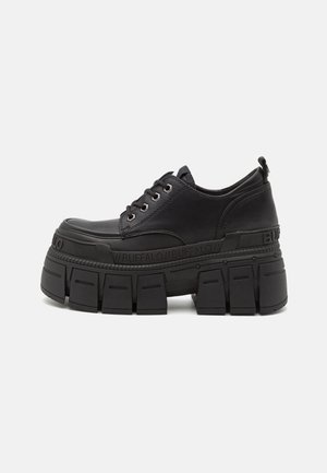Chaussure plateforme noire à semelle épaisse et rainurée, fermeture à lacets sur l'avant, avec la marque "BUFFALO" sur la semelle intermédiaire et la languette talonnière.