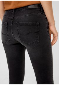 Melni denim džinsi ar piegulošu dizainu, vidēju jostas augstumu un divām aizmugurējām kabatām, kurām ir izliekta šuvju apdare un ādas logo uzlīme.