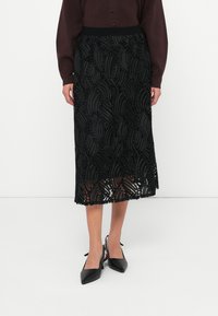 Μαύρη μίντι φούστα με στρωματωμένα, υφασμένα φύλλα και φριριστές άκρες. Έχει εφαρμοστό μέσον και διάφανο, ρέον ύφασμα.