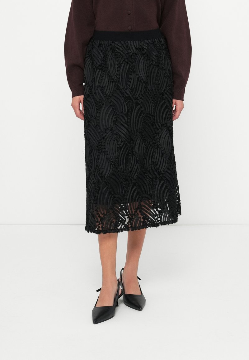 Μαύρη μίντι φούστα με στρωματωμένα, υφασμένα φύλλα και φριριστές άκρες. Έχει εφαρμοστό μέσον και διάφανο, ρέον ύφασμα.