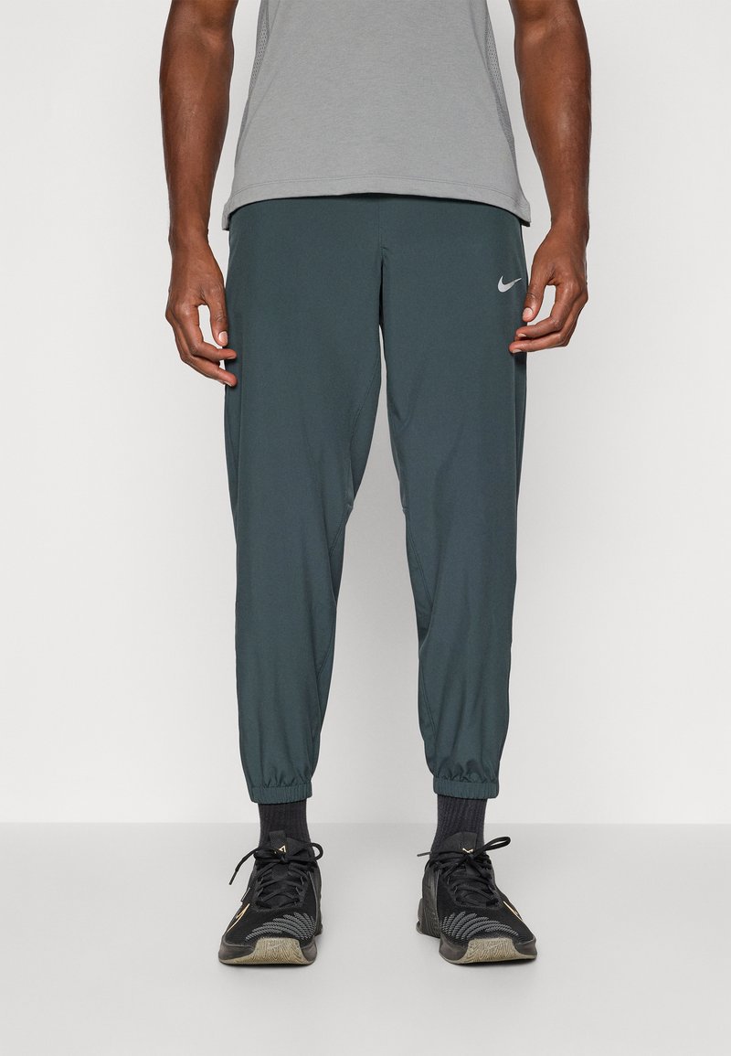 Pantaloni atletici ușori, de culoare verde închis, cu picioare îngustate și manșete elastice, având un mic logo argintiu Nike pe piciorul stâng.