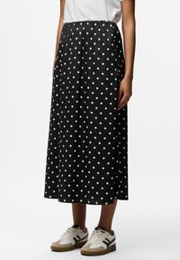 Mustreeritud must midi-seelik, millel on kokku volditud vöökoht, valmistatud siledast kangast. Kombineeritud valgete spordijalatsitega, millel on beežid ja maroonid aktsendid.