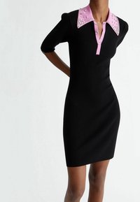 Robe noire à rayures avec manches courtes, col rose orné de clous et patte de boutonnage à cinq boutons. Design ajusté.