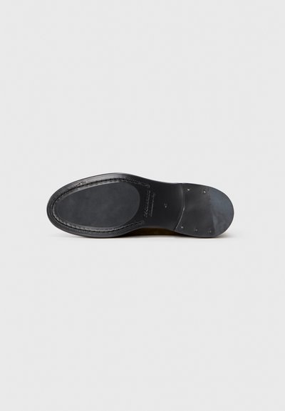 Semelle de chaussure en cuir noir avec une finition lisse, une forme arrondie et des accents en métal. Présente des coutures le long du bord et une base plate.