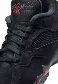 Baskets noires en matériau daim, avec des accents en mesh, de grosses lacets et un logo rouge. Design courbé avec des perforations et une semelle en caoutchouc.