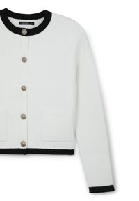 Weißer Cardigan mit schwarzem geripptem Kragen und Bündchen, versehen mit silbernen Knöpfen vorne und zwei aufgesetzten Taschen. Weiche Textur.