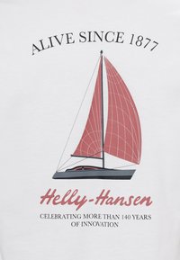Bílá tričko s grafikou jachty s červenými plachtami, černým trupem a textem "Živý od 1877" a "Helly-Hansen."
