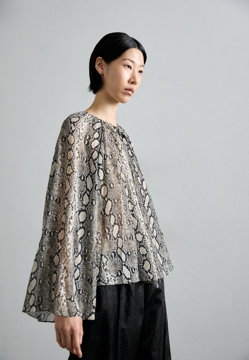 Lichte, doorschijnende blouse in een slangenprintpatroon met tinten beige en zwart; heeft bell mouwen en een ronde halslijn.
