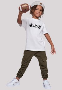 White cotton t-shirt with black graphic design, olive green cargo pants with side pockets, and white sneakers with silver accents.