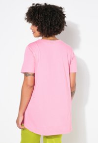 Camiseta rosa de manga corta con escote redondo, hecha de material suave. El dobladillo es ligeramente más largo por detrás, con una textura suave.
