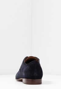 Chaussures en daim marine avec un bout arrondi et une semelle en cuir brun lisse. Le design présente une couture minimale et une silhouette épurée.