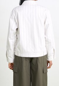 Bílý pruhovaný sako z tkaniny s hladkou texturou, s rovný střihem, zapínáním na cvoky a manžetami na knoflíky.