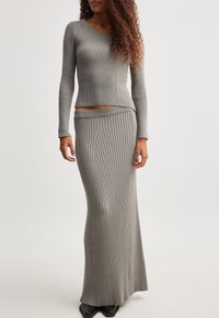 Completo a due pezzi in maglia grigia a coste con top aderente a maniche lunghe e gonna a vita alta, caratterizzato da una silhouette elegante e allungata.