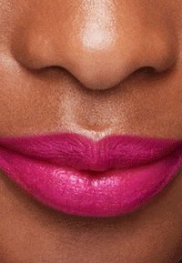Nærbilde av fyldige lepper med en glossy, livlig fuchsia leppestift, satt mot en middels brun hudtone, med en jevn tekstur.