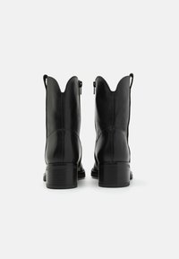 Botas de cuero negro hasta el tobillo con punta afilada, cremalleras laterales y tacón apilado. Textura suave con sutiles detalles de costura.