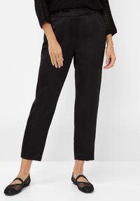 Zwarte, rechte broek van een gevarieerde stof, met zijzakken en een elastieken tailleband. Gecombineerd met zwarte gevlochten ballerina's.