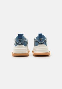 Denim sneakers with a white and orange sole, featuring frayed edges and a blue loop tab. Back view showing distinct styling and textures.