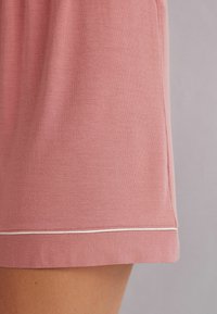 Ljust rosa bomullsshorts med en slät textur, en enkel design och en kontrasterande vit söm längs fållen.