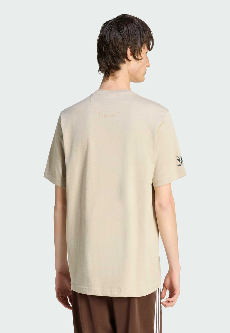 Maglietta beige in cotone con maniche corte, scollo rotondo e piccolo dettaglio logo nero sulla manica sinistra. Design semplice e vestibilità comoda.