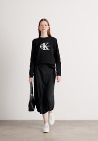 Juodas ilgomis rankovėmis palaidinė su logotipu, derinama su plevenčia juoda sijonu. Balti sportbačiai ir juoda rankinė užbaigia aprangą.