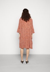 Vestido floral vermelho com um design em camadas e mangas largas. Feito de um material leve, apresentando um pequeno padrão de flores dispersas.