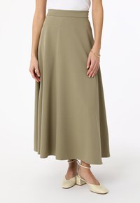 Jupe kaki jusqu'aux genoux en tissu doux avec une texture lisse. Présente une taille ajustée et un design évasé, assortie à des chaussures à talons carrés crème.