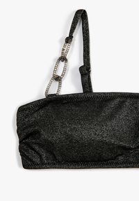 Schwarzes trägerloses Top aus strukturiertem, schimmerndem Stoff, mit einem gerafften Design und einem Kettenlinkakzent an einem Träger.